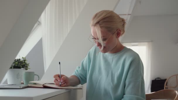 Όμορφη νεαρή γυναίκα γράφει κάτι στο σημειωματάριο, ενώ εργάζεται στο γραφείο — Αρχείο Βίντεο