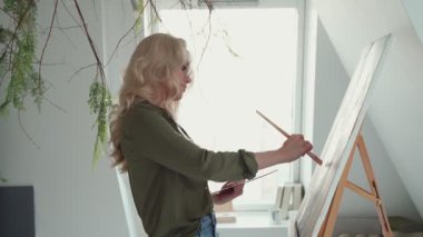 Sanat stüdyosunda resim yapan çekici genç bir kadının yan görünüşü 