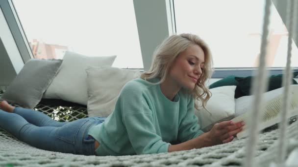Όμορφη νεαρή γυναίκα διαβάζει το βιβλίο και χαμογελώντας ενώ χαλαρώνει στη μεγάλη αιώρα — Αρχείο Βίντεο
