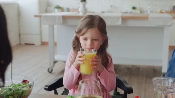 Glad liten flicka njuter av juice och leende medan du äter middag med familjen — Stockvideo