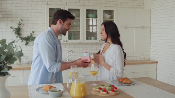 Ung man ger en presentask till sin flickvän medan han äter frukost — Stockvideo