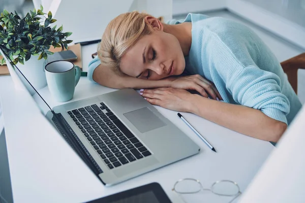 Draufsicht auf müde junge Frau, die an ihrem Arbeitsplatz im Büro schläft — Stockfoto