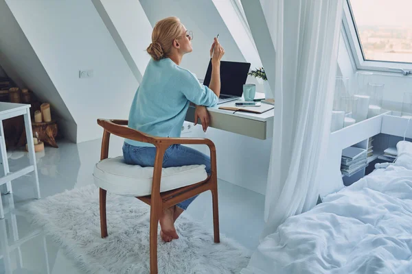 Mooie jonge vrouw op zoek bedachtzaam tijdens het werken thuis — Stockfoto