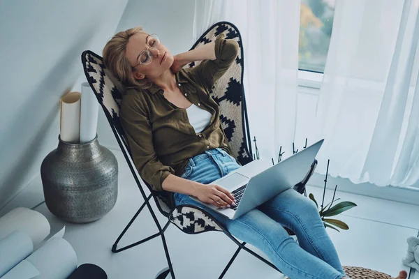 Moe jonge vrouw dragen laptop en het houden van ogen gesloten terwijl zitten in comfortabele stoel thuis — Stockfoto