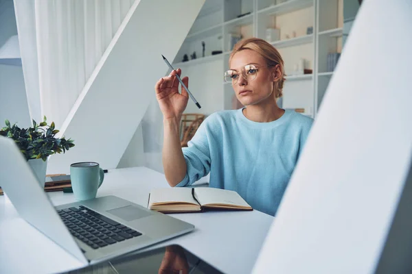 Schöne junge Frau sieht nachdenklich aus, während sie zu Hause arbeitet — Stockfoto