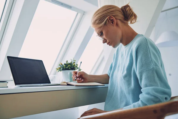 Piękna młoda kobieta pisząca coś w notatniku podczas pracy w biurze — Zdjęcie stockowe