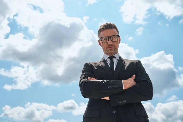 Lage hoek uitzicht van zelfverzekerde volwassen man in volle pak houden armen gekruist — Stockfoto