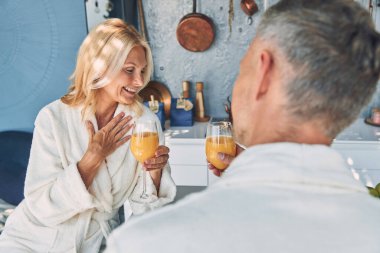 Bornozlu güzel, olgun bir çift evcil mutfakta vakit geçirirken taze meyve suyunun tadını çıkarıyor.