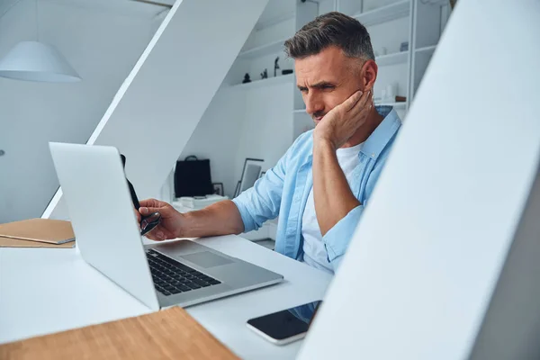 Fatigué homme mûr travaillant sur ordinateur portable tout en étant assis au bureau — Photo