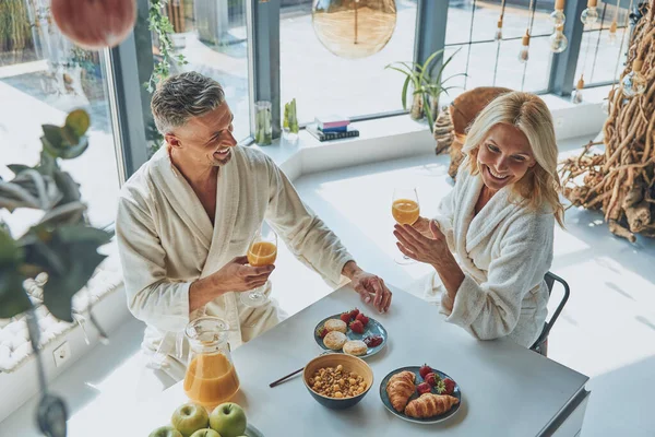 Vista dall'alto di una bella coppia matura in accappatoi che gusta la colazione insieme mentre trascorre del tempo in cucina domestica — Foto Stock