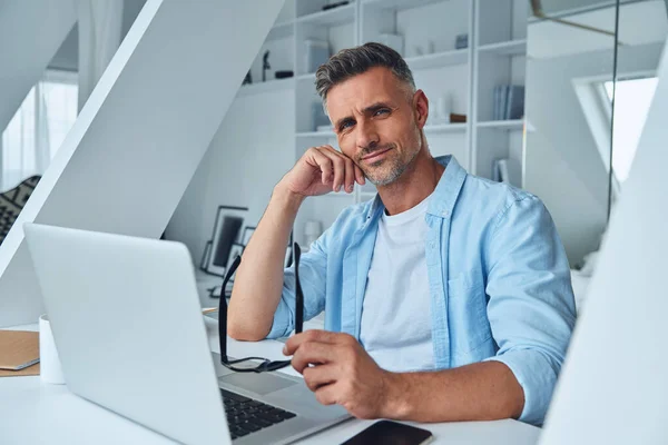 Homme mature confiant regardant la caméra alors qu'il était assis au bureau — Photo