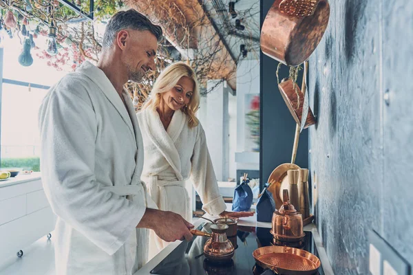 Beautiful mature couple in bathrobes preparing coffee together while spending time in the domestic kitchen — Stock Photo, Image