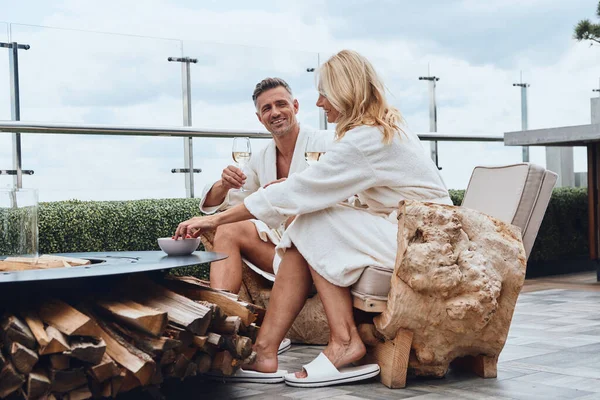 Hermosa pareja madura en albornoces disfrutando de frutas y champán mientras se relaja en un hotel de lujo al aire libre —  Fotos de Stock