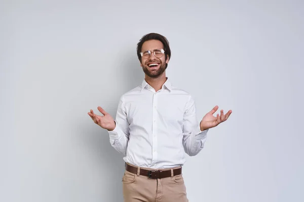 Bello giovane uomo sorridente in camicia bianca gesticolando mentre in piedi su sfondo grigio — Foto Stock