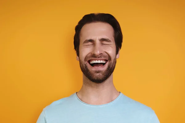 Retrato de jovem feliz em roupas casuais mantendo os olhos fechados enquanto em pé contra o fundo amarelo — Fotografia de Stock