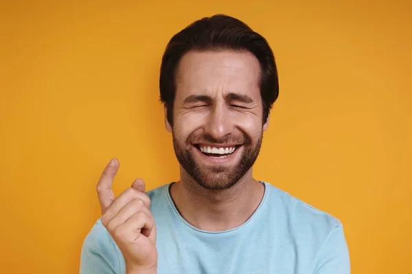 Retrato de un joven sonriente con ropa casual haciendo gestos de pequeño tamaño mientras está de pie sobre un fondo amarillo — Foto de Stock