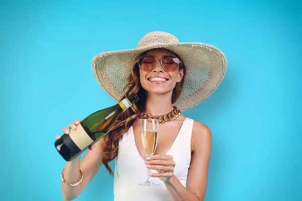 Hermosa mujer joven en elegante sombrero vertiendo champán en la copa y sonriendo —  Fotos de Stock