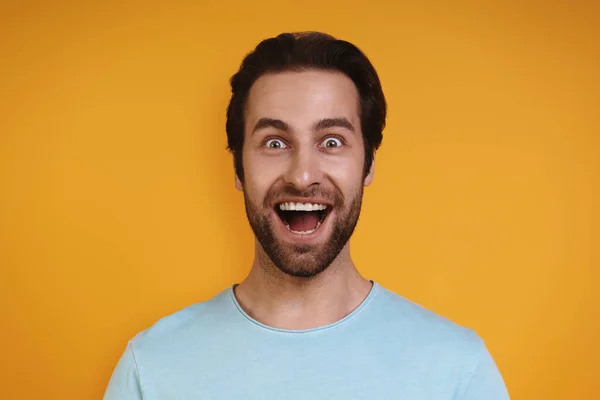 Porträt eines aufgeregten jungen Mannes in lässiger Kleidung, der vor gelbem Hintergrund in die Kamera blickt und lächelt — Stockfoto