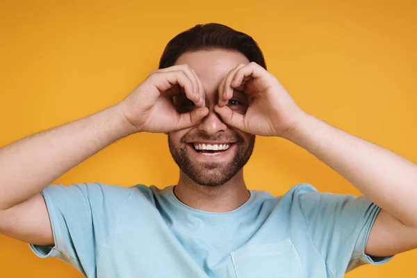 Portrait curieux jeune homme en vêtements décontractés gesticulant lunettes et souriant tout en se tenant debout sur fond jaune — Photo