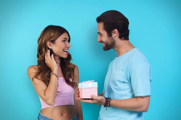 Guapo joven dando una caja de regalo a su novia, mientras que de pie sobre fondo azul —  Fotos de Stock