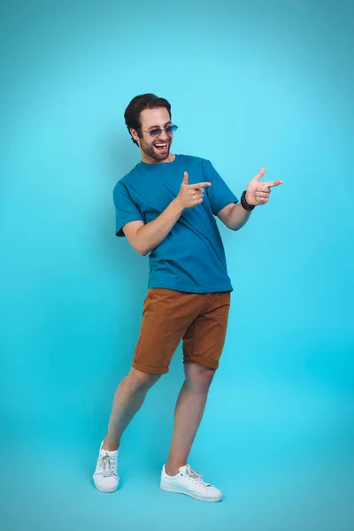 Beau jeune homme en vêtements décontractés gesticulant et souriant tout en se tenant debout sur fond jaune — Photo