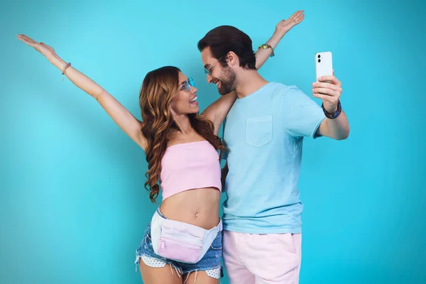 Krásný mladý usmívající se pár dělat selfie zatímco stojí na modrém pozadí — Stock fotografie