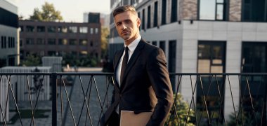 Ofis binalarının yanında dizüstü bilgisayar taşıyan kendine güvenen olgun bir adam.