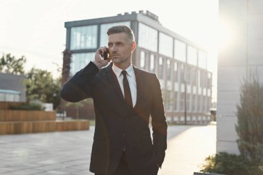 Ofis binasının yanında yürürken cep telefonuyla konuşan kendinden emin bir iş adamı.