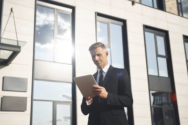 Homme d'affaires mature confiant tenant tablette numérique tout en se tenant près de l'immeuble de bureaux — Photo