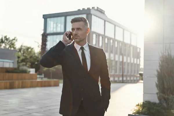 Självsäker mogen affärsman talar på mobiltelefon när du går nära kontorsbyggnad — Stockfoto