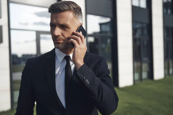 Selbstbewusster reifer Geschäftsmann telefoniert in der Nähe von Bürogebäuden — Stockfoto