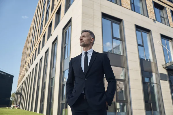 Zelfverzekerde volwassen zakenman die voor het kantoorgebouw buiten staat — Stockfoto