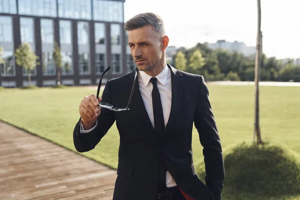 Confident mature businessman carrying his eyeglasses while standing outdoors — Stock Photo, Image