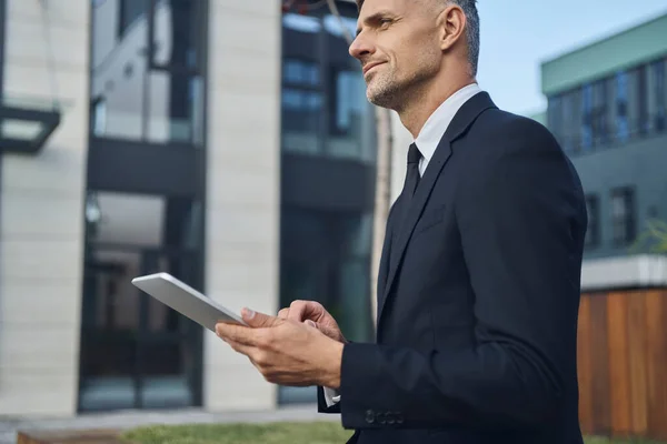 Jistý zralé podnikatel pomocí digitálního tabletu, zatímco stojí venku v blízkosti kancelářské budovy — Stock fotografie