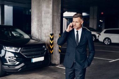 Otoparkta yürürken cep telefonuyla konuşan kendinden emin bir iş adamı.