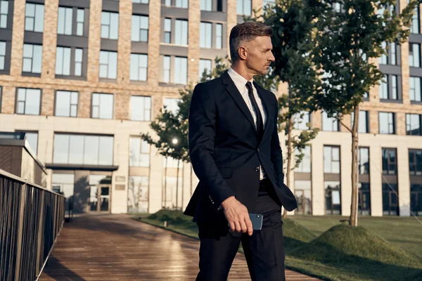 Zelfverzekerde volwassen zakenman loopt buiten met kantoorgebouw op de achtergrond — Stockfoto