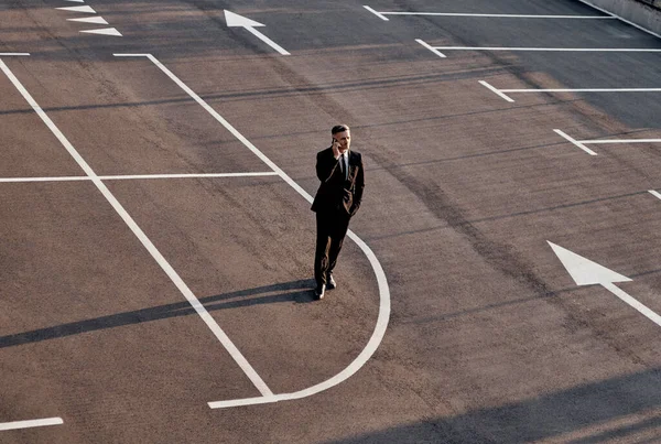 Vista superior del hombre en ropa formal hablando en el teléfono móvil, mientras que de pie en el estacionamiento con el signo de flecha en él —  Fotos de Stock