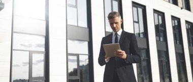 Ofis binasının yanında dikilirken elinde dijital tablet tutan kendinden emin bir iş adamı.