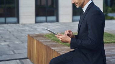 Ofis binasının yanında otururken dijital tablet kullanan kendinden emin bir iş adamı.