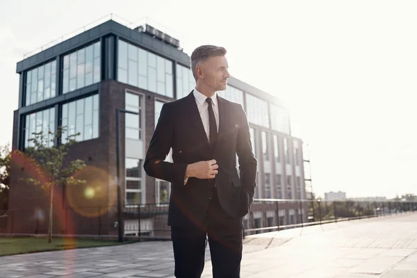 Homme d'affaires mature confiant ajustant son costume tout en se tenant près de l'immeuble de bureaux à l'extérieur — Photo