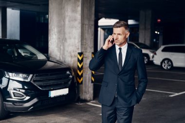 Otoparkta yürürken cep telefonuyla konuşan kendinden emin bir iş adamı.