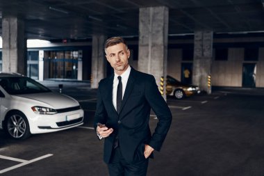Otoparkta yürürken cep telefonu taşıyan kendinden emin bir iş adamı.