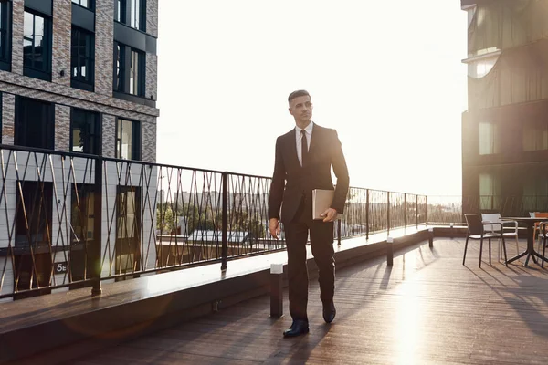 Homem maduro confiante em terno completo carregando laptop enquanto caminhava pelo terraço do centro de negócios ao ar livre — Fotografia de Stock