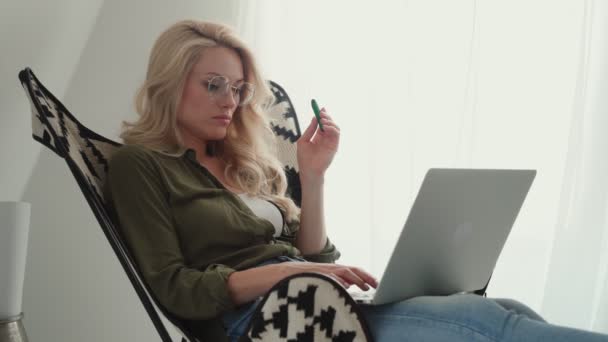 Νεαρή γυναίκα που χρησιμοποιεί φορητό υπολογιστή και ηλεκτρονικό τσιγάρο ενώ χαλαρώνει στο σπίτι — Αρχείο Βίντεο