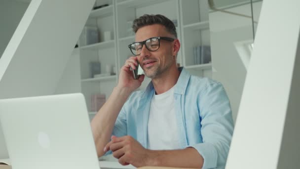 Ώριμος άντρας που δουλεύει σε λάπτοπ και μιλάει στο τηλέφωνο ενώ κάθεται στο γραφείο — Αρχείο Βίντεο