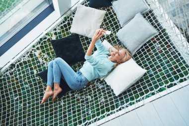 Güzel genç bir kadının akıllı telefonuyla selfie çekerken evdeki büyük hamakta dinlendiği en güzel manzara.