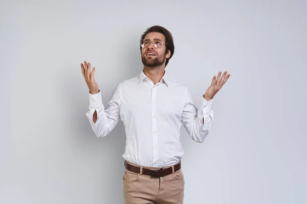 Handsome young man in white shirt looking at camera and gesturing while standing against gray background — Stock Photo, Image