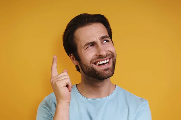 Retrato de jovem feliz em roupas casuais gesticulando e olhando para longe enquanto estava de pé contra fundo amarelo — Fotografia de Stock