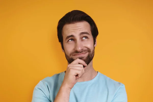 Porträt eines jungen Mannes in lässiger Kleidung, der die Hand am Kinn hält und vor gelbem Hintergrund wegschaut — Stockfoto