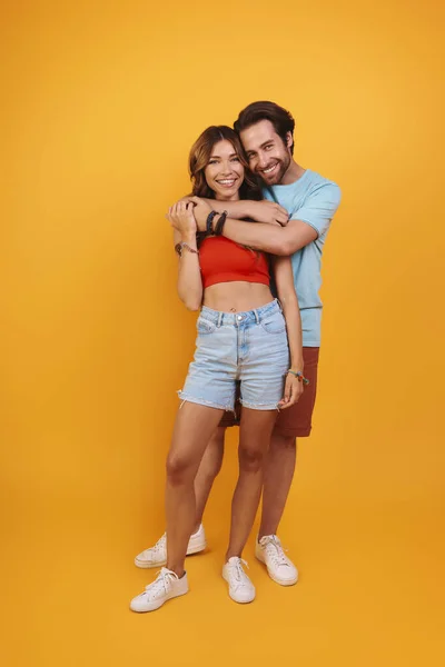 Full length of beautiful young couple embracing while standing against yellow background — Stock Photo, Image